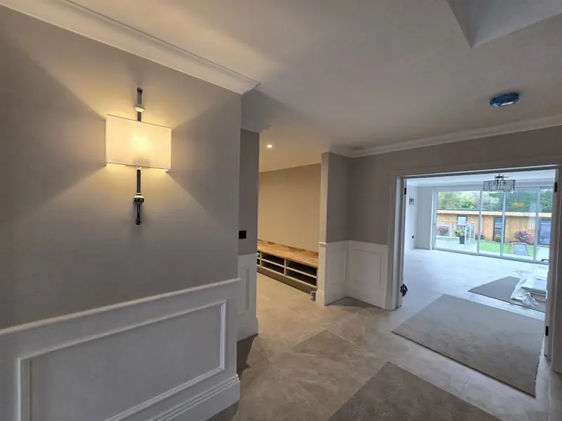 Hallway with panelled walls, wall lights and a tiled floor leading to glazed doors