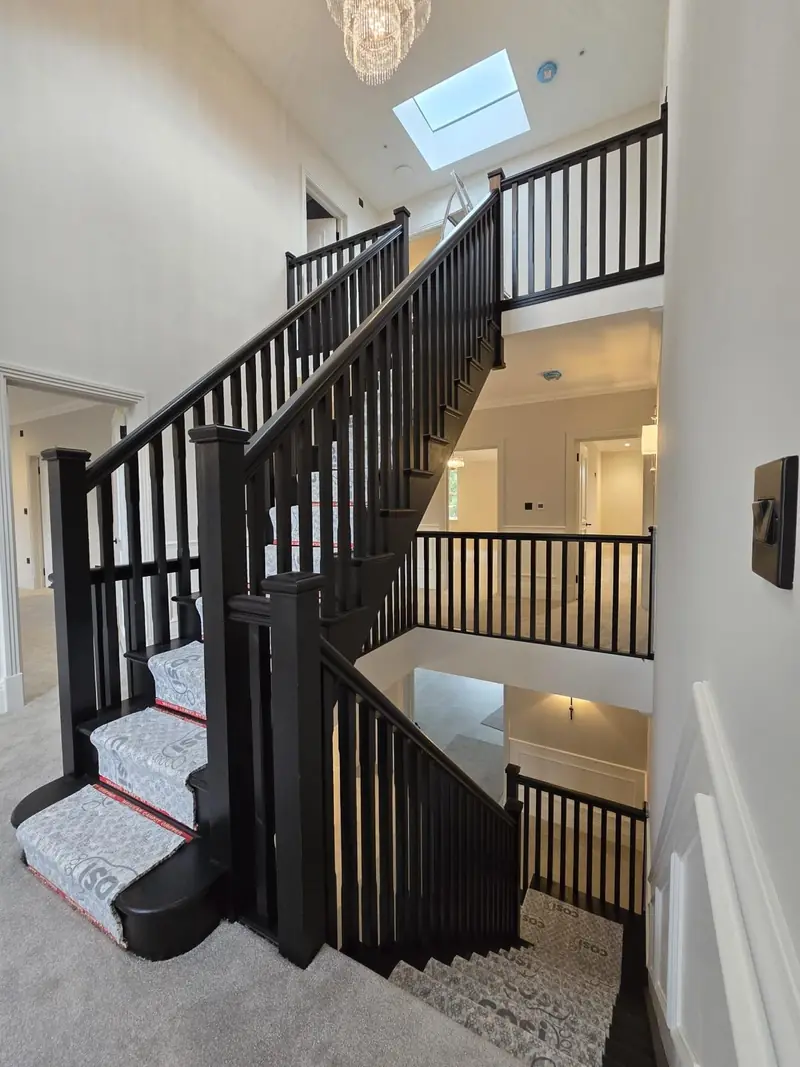 Staircase with black spindles and a carpet runner rising to a landing lit by a rooflight
