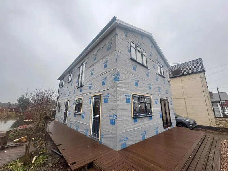 Two-storey house under construction, wrapped in breather membrane, with windows fitted and a deck
